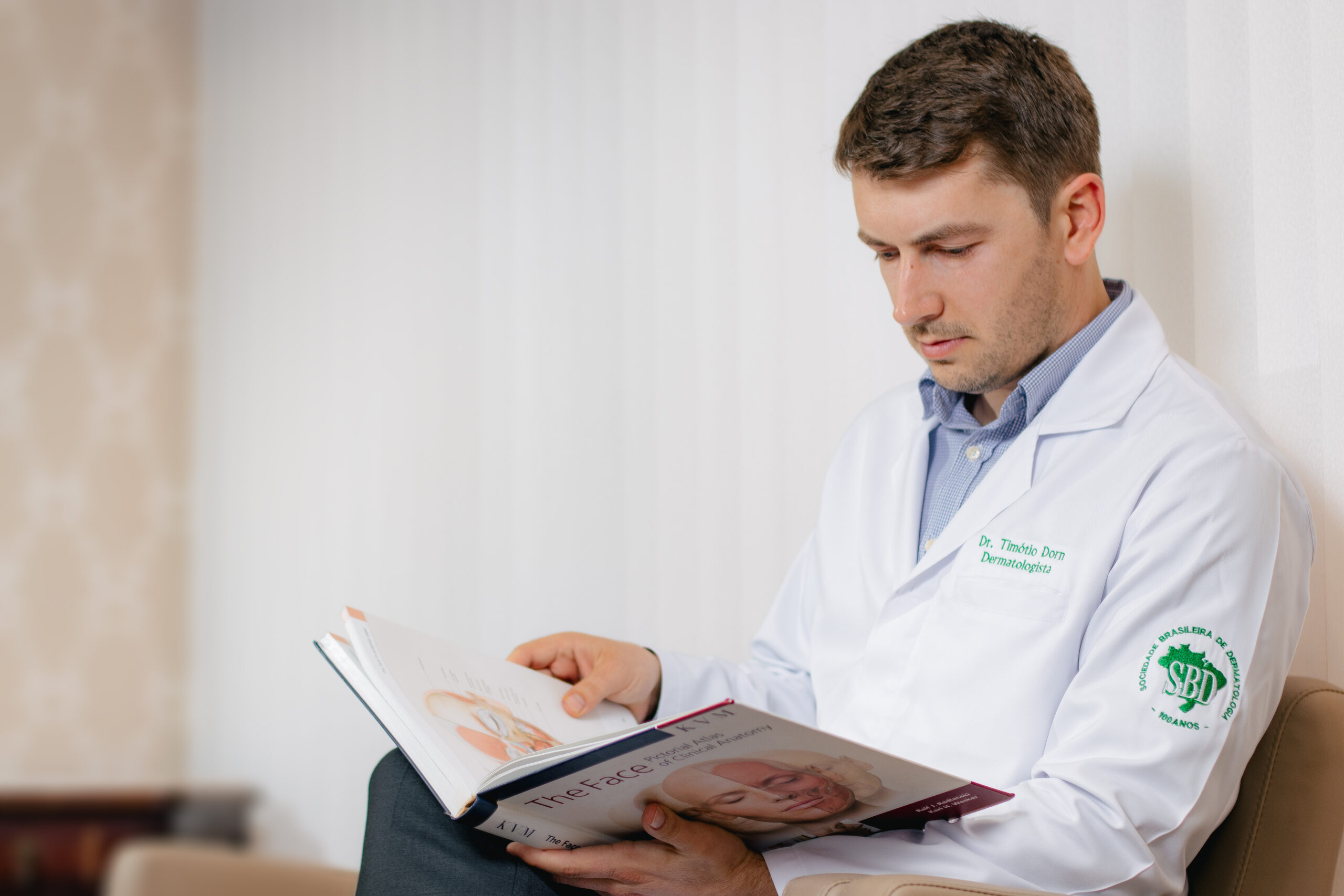 Dermatologista consulta literatura especializada em cirurgia de Mohs e reconstrução facial para planejamento do tratamento do câncer de pele.