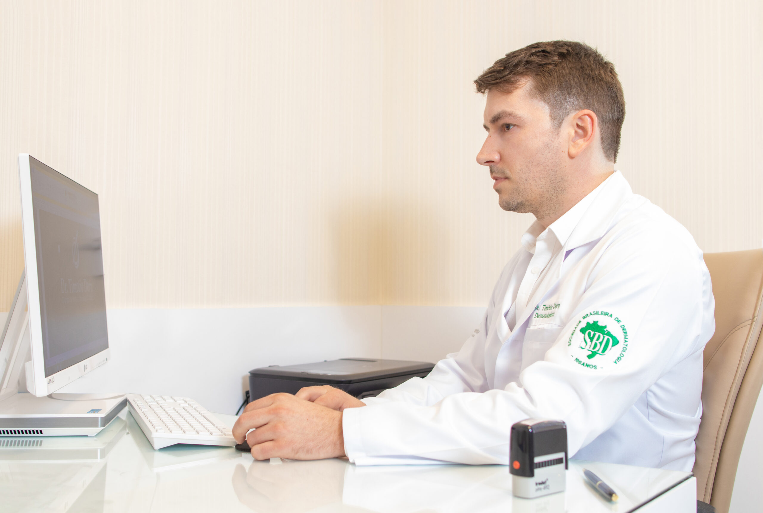 Dr. Timótio Dorn em atendimento no consultório, utilizando computador para avaliação clínica e planejamento de tratamentos dermatológicos.