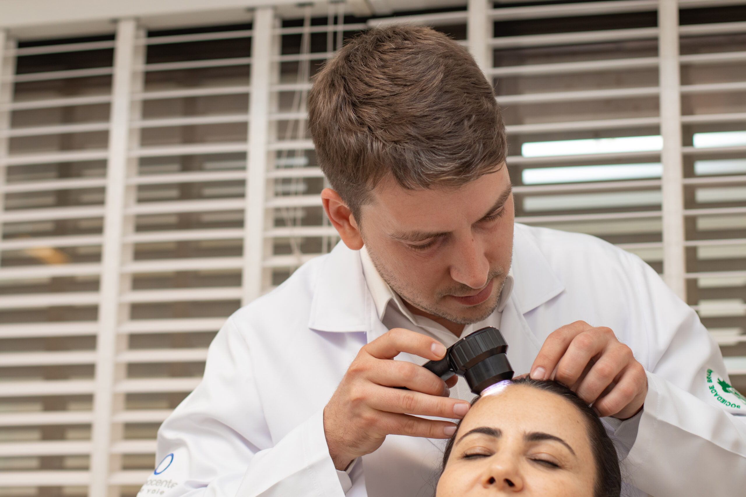 Dermatologista realiza exame dermatoscópico no couro cabeludo da paciente para avaliação de lesão cutânea antes da cirurgia de Mohs.